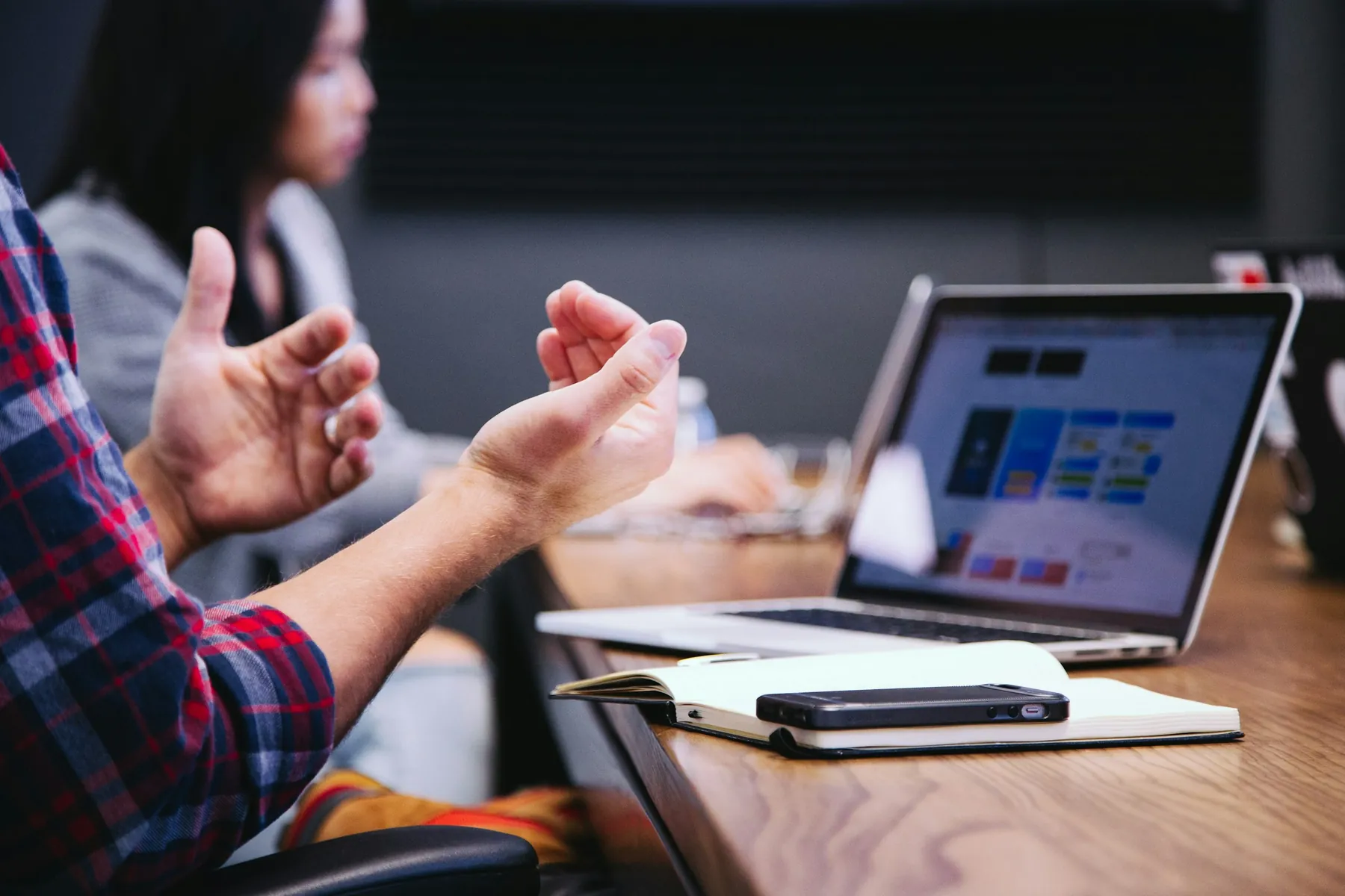 A person gesturing while talking with colleagues over an open laptop.