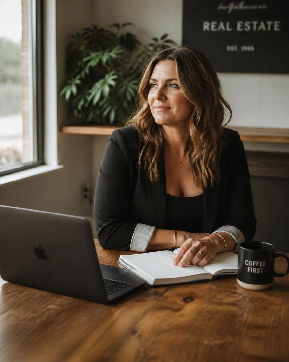 An independent real estate professional working at a sunlit wooden table with a laptop and open notebook.