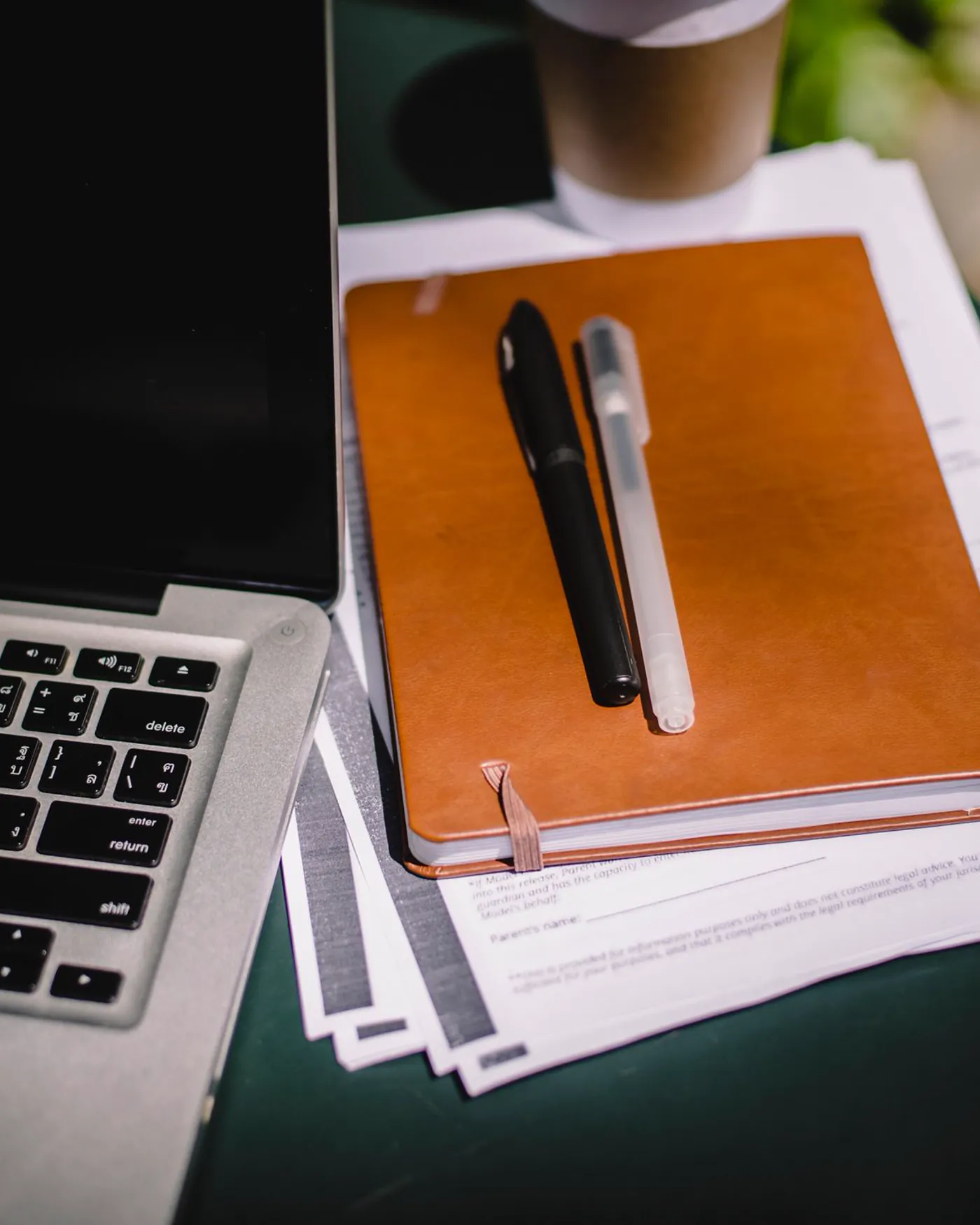 Overhead view of an open planner, pens, a laptop and a cup of coffee on a desk.