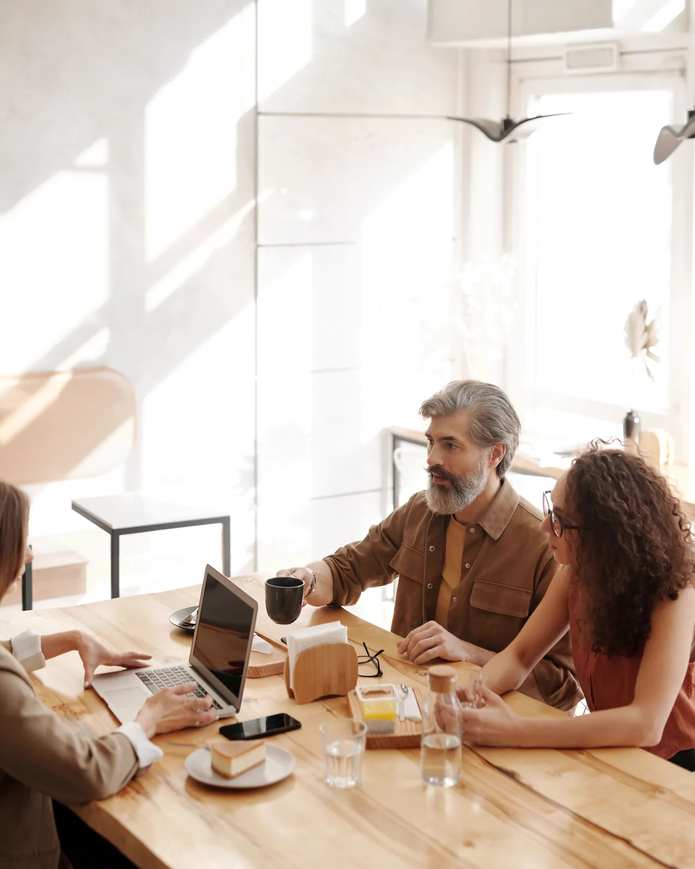 A small group of people talking together around a table in a sunlit coffee shop.
